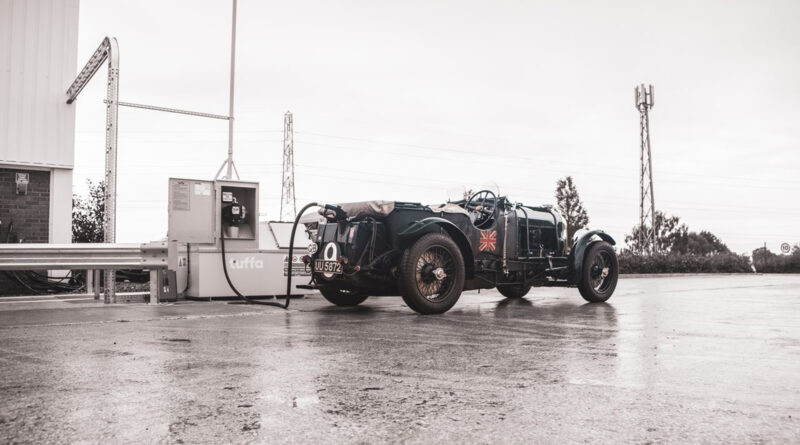 A black and white photo of an old car parked at a gas station.